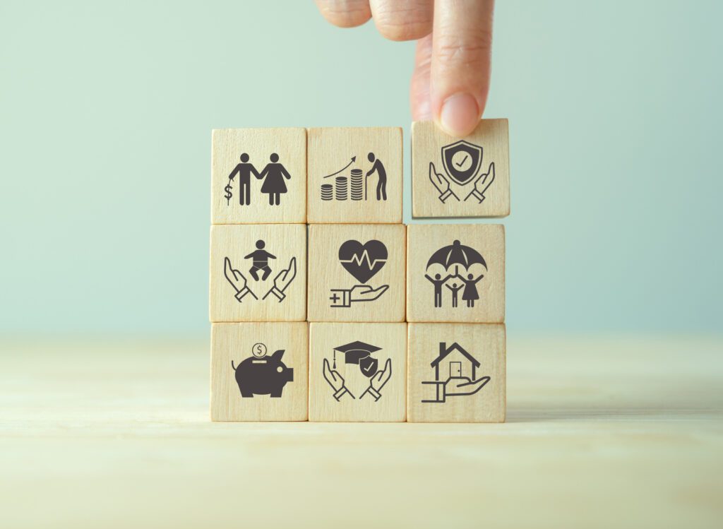 Insurance and stages of life concept. Hand puts wooden cube with assurance icon standing on finance, education, real estate and property, health, child, family and pension planing icon, smart banner