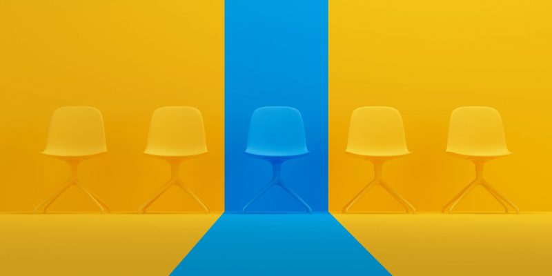 Blue chair that stands out from the crowd of chairs against a yellow studio background. Human resource management concept. Blue chair that stands out from the crowd of chairs against a yellow studio background. Human resource management concept.